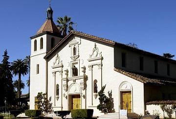 A white mission-style church with a tower under a clear blue sky.