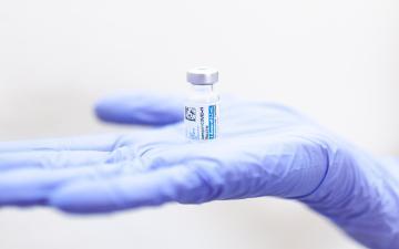 A gloved hand holding a vial labeled 