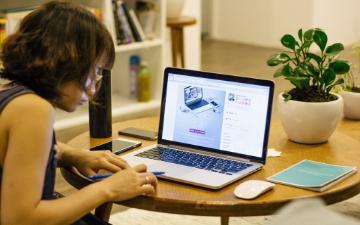 woman at table containing an open laptop, mouse, pen, and houseplant