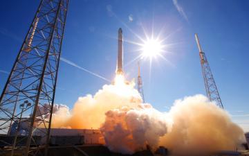 Alt text: Rocket launching with smoke and flames under a clear blue sky.