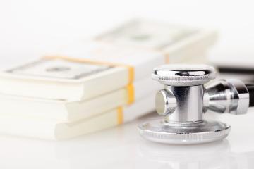 Stethoscope next to stacks of hundred dollar bills.