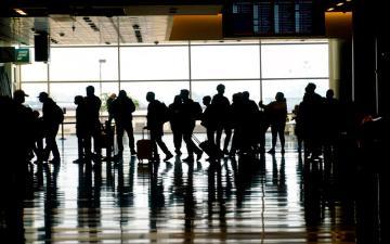 Silhouetted travelers with luggage walking through an airport.