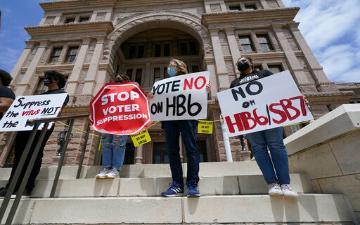 People holding signs protesting against the voter bill on a building's steps.