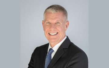 A person in a suit smiling against a light gray background.