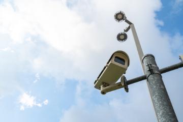 Surveillance cameras mounted on a pole against a cloudy sky backdrop.