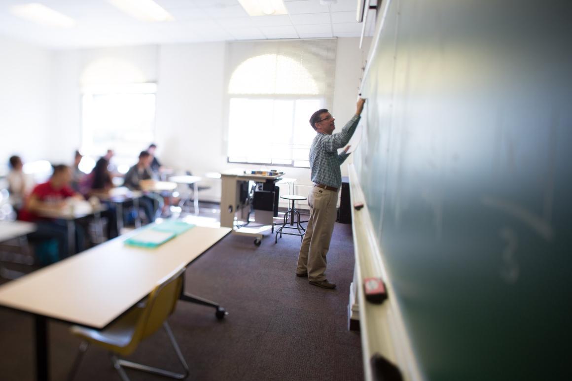 A teacher writing on a chalkboard while students watch.
