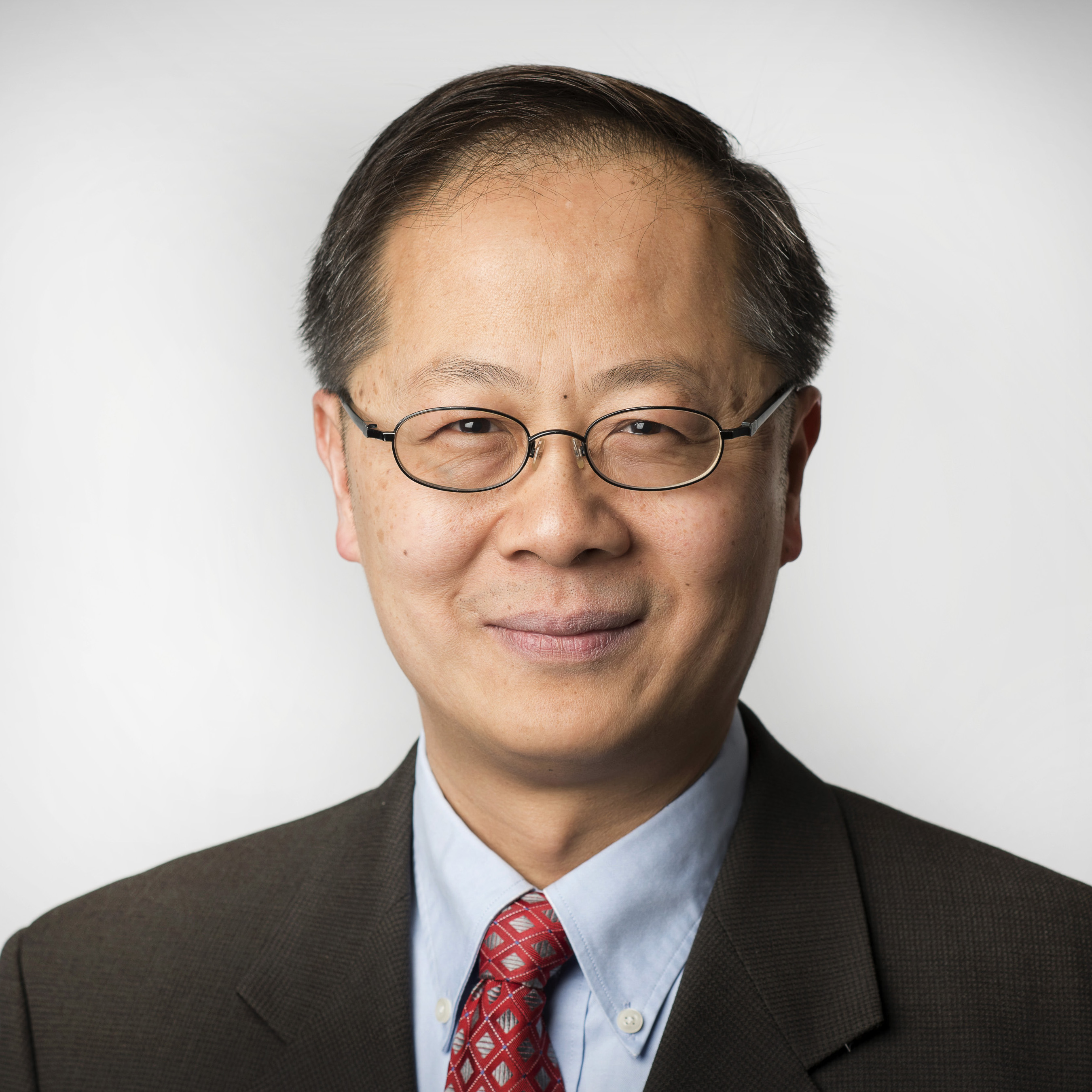 A person wearing glasses, a suit, and a red tie.