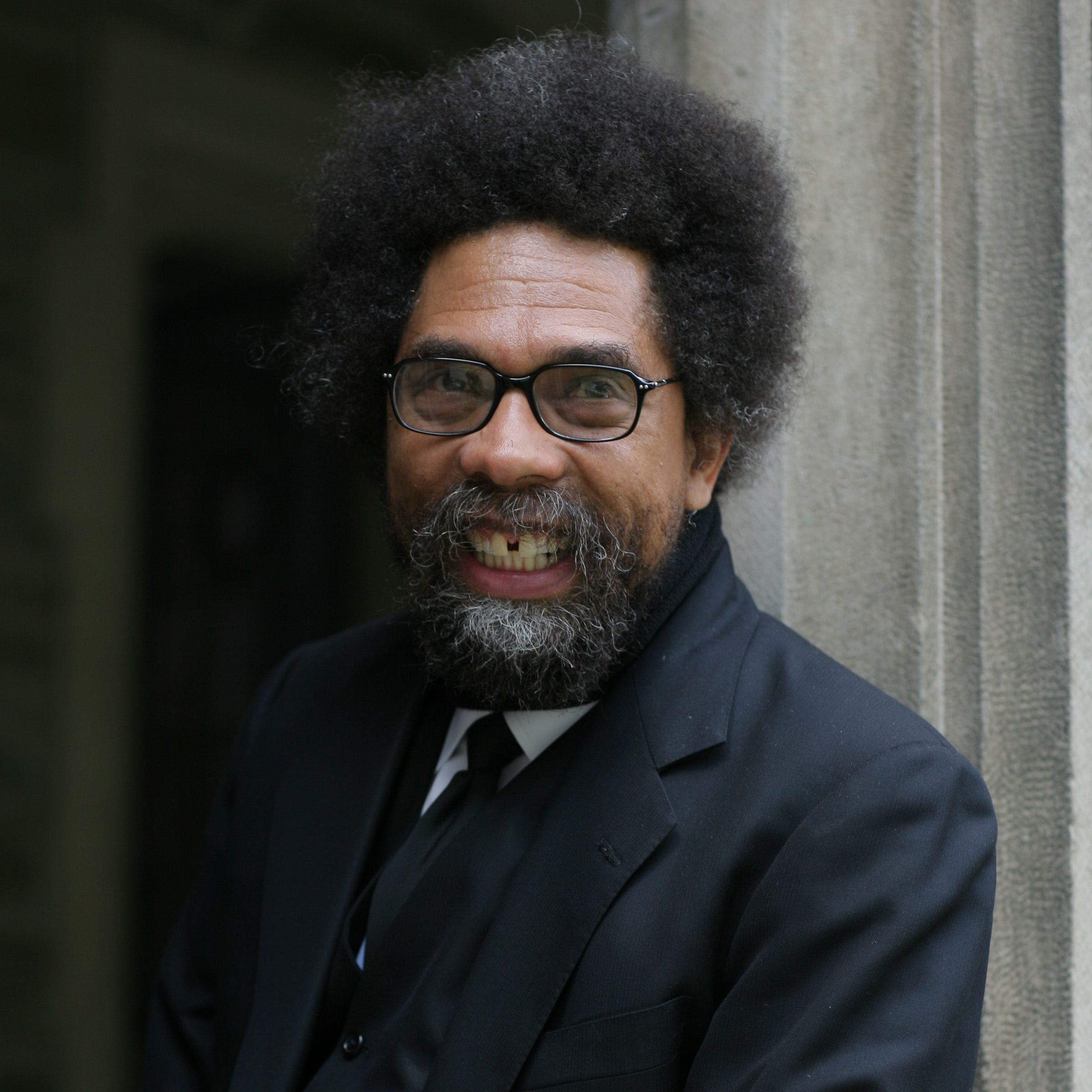 Cornel West smiling wearing a dark suit and tie.