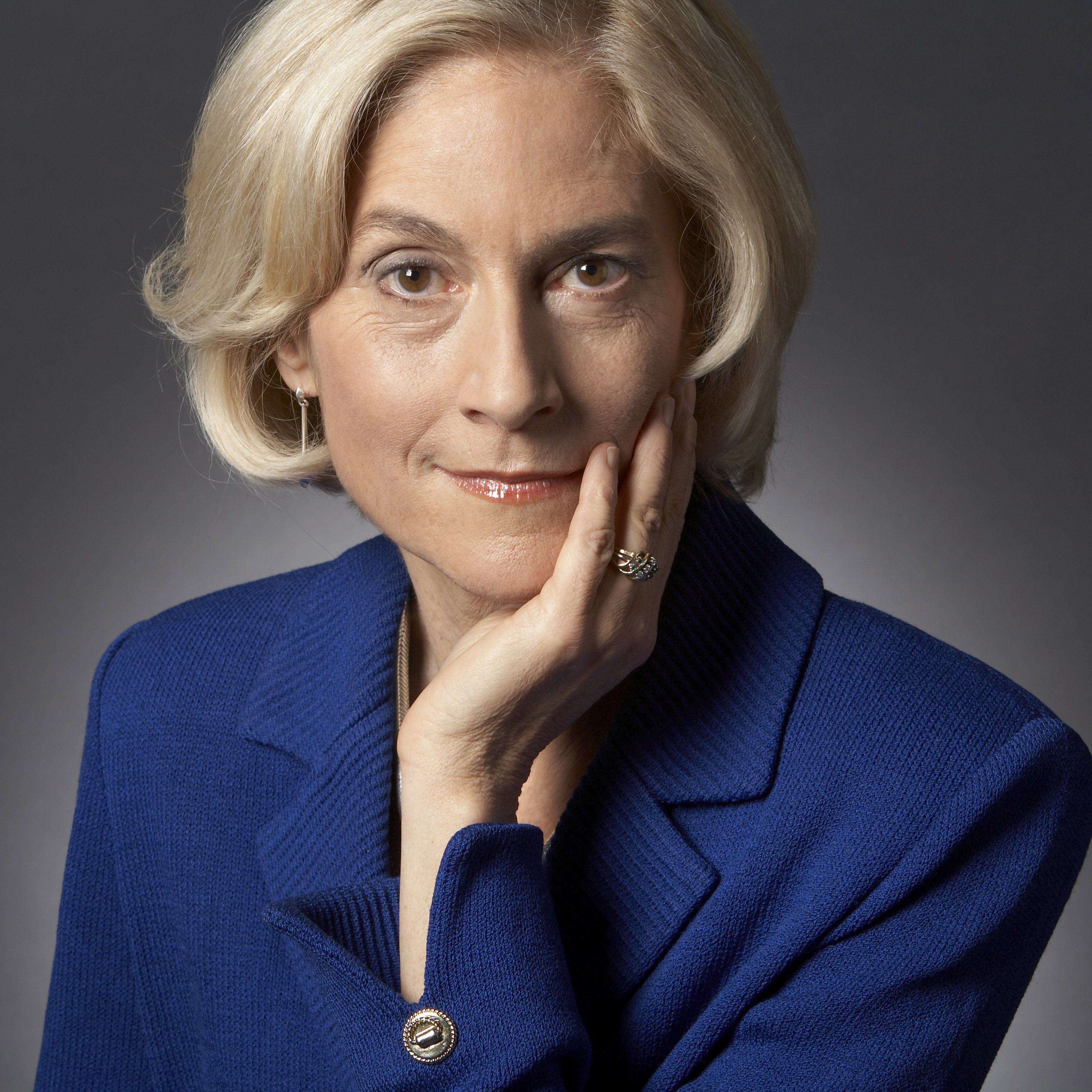 A woman in a blue blazer resting her chin on her hand.