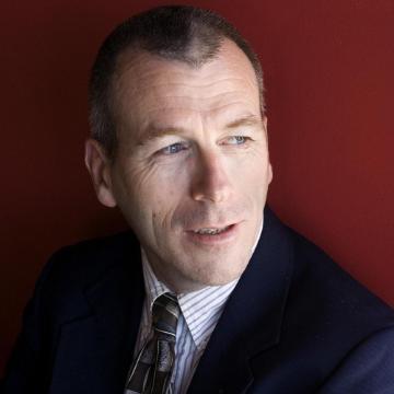 A person in a suit looking to the side against a red background.