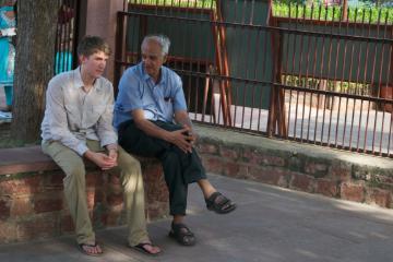 Two people sitting on a bench outdoors, engaged in conversation.