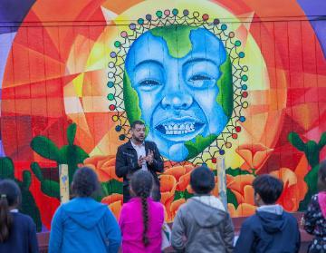 A person speaking to a small crowd in front of a colorful mural. image link to story