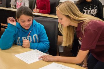 A teacher assists a student with classroom work at a desk.