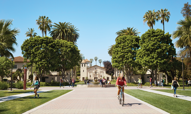 People walking on a tree-lined campus path with a building in the background.