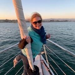 Person on a boat holding a sail, smiling at sunset.