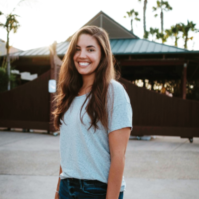 A person smiling in an outdoor setting with palm trees.