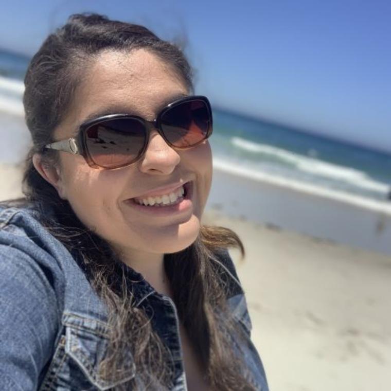 A woman smiling on a beach wearing sunglasses.