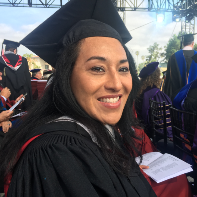 A person in graduation attire smiling at an outdoor ceremony.