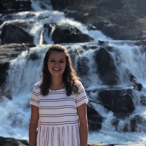 Person standing in front of a waterfall, wearing a white and striped dress.