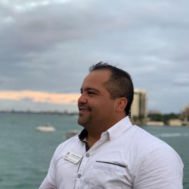 A person smiling with a waterfront and cityscape in the background.