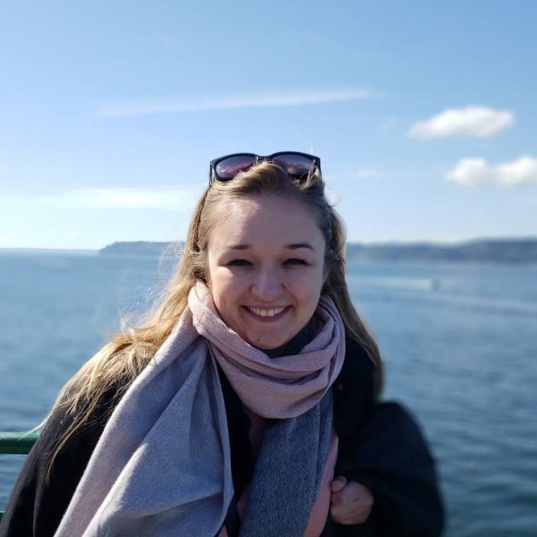 Person smiling in front of a body of water and sky.