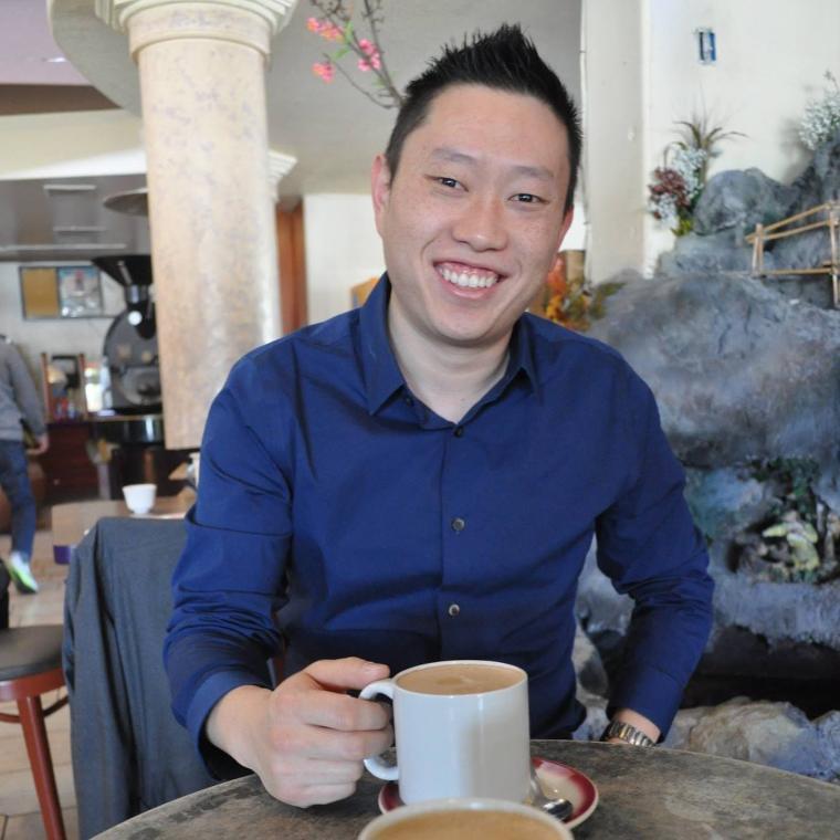 Person holding a mug, sitting at a table, smiling.