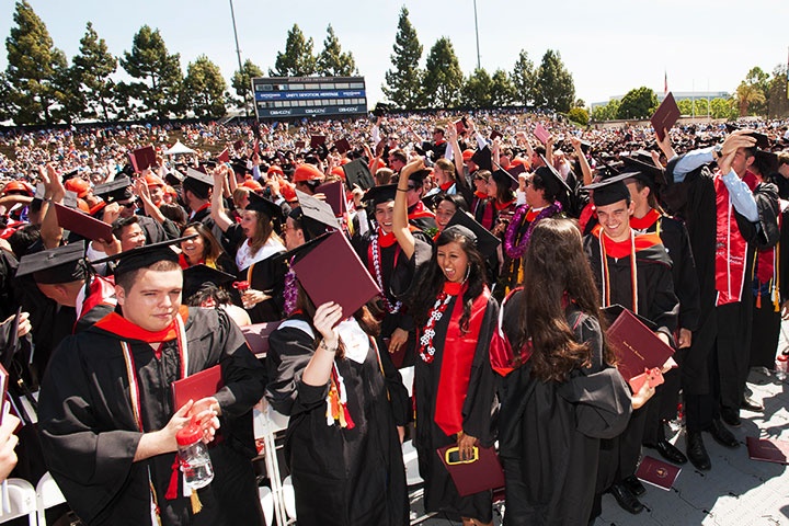 A large crowd of graduates in caps and gowns at an outdoor commencement ceremony. image link to story