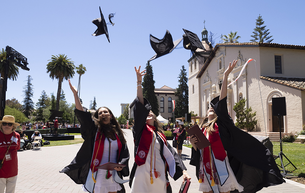 Three female graduates toss their caps in the air alongside Mission Church image link to story