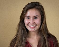 Smiling person in a maroon top with a neutral background.