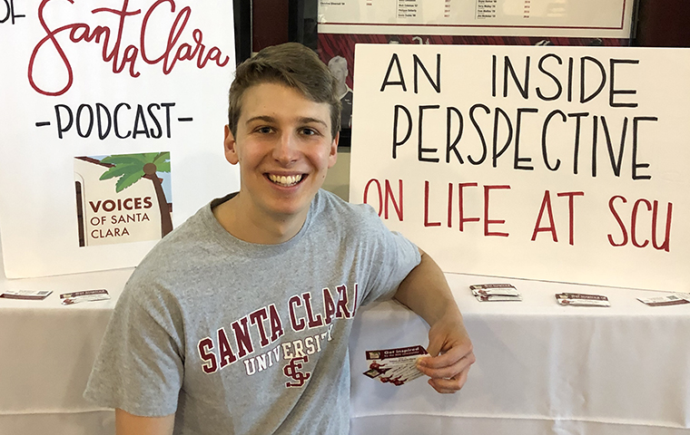 Gavin Cosgrave sitting in front of poster boards for his Voices of Santa Clara podcast