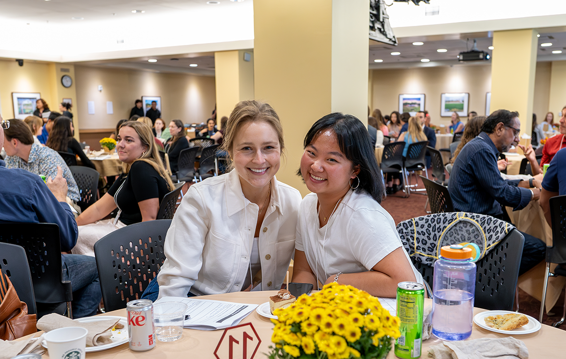 Two women pose at a table at a dinner event.