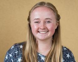 A person smiling against a yellow background.