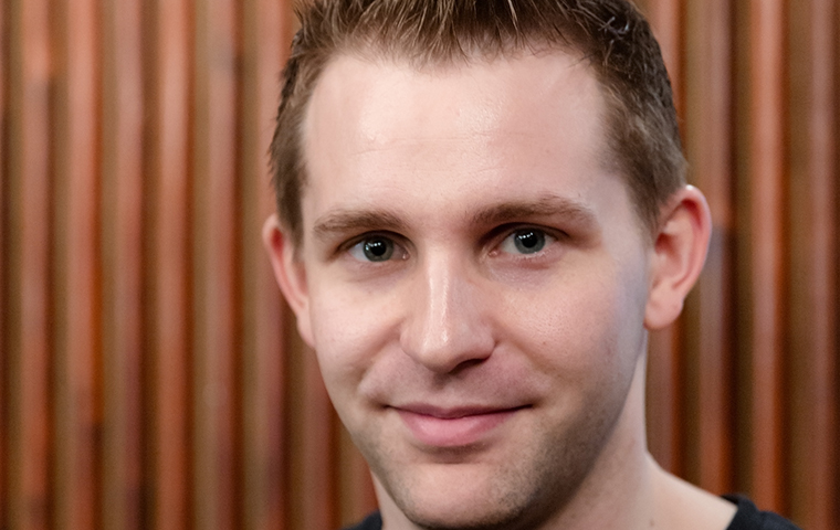 A man smiling in front of a wooden background.