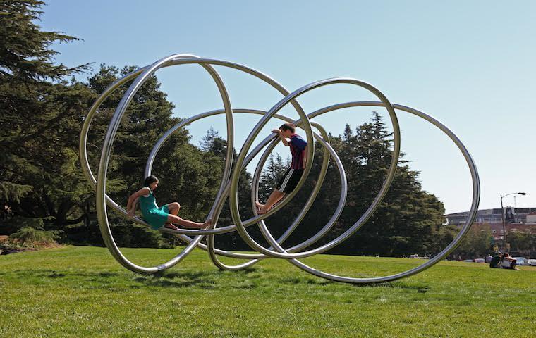 Large metallic rings placed in a grassy outdoor area. image link to story