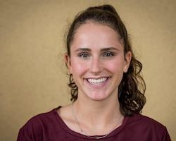 A smiling person with a light brown background.