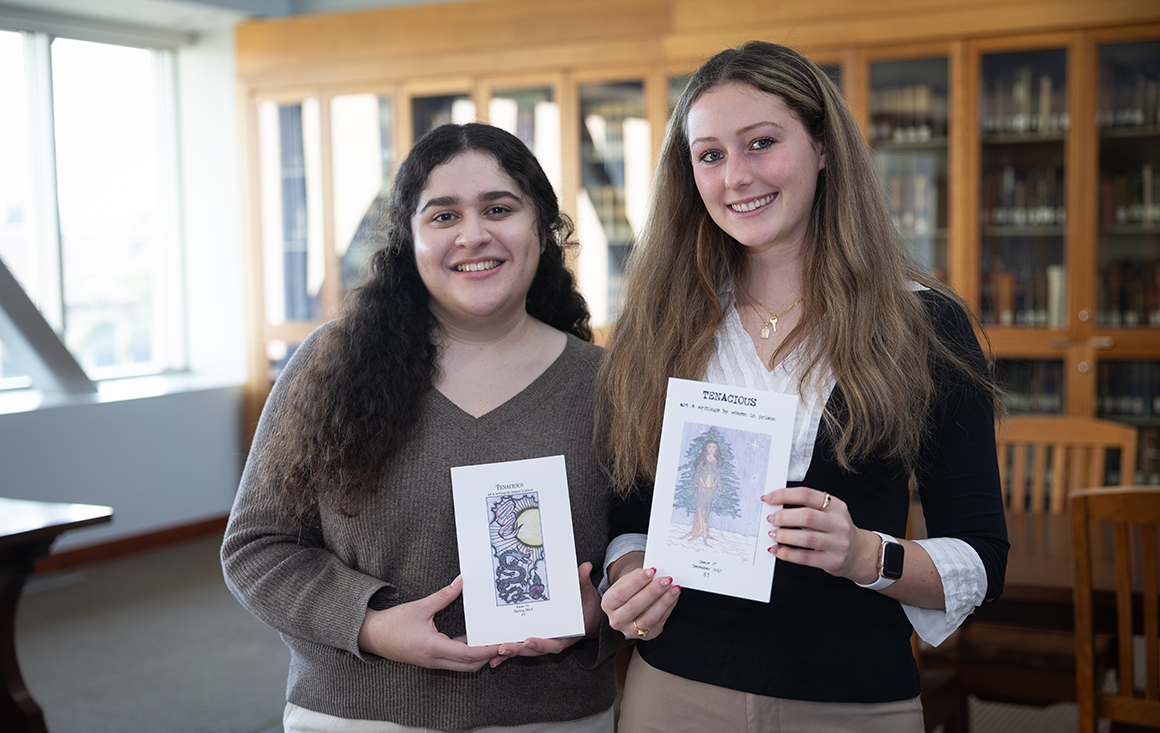 Two female students pose holding issues of the Tenacious Zine collection.