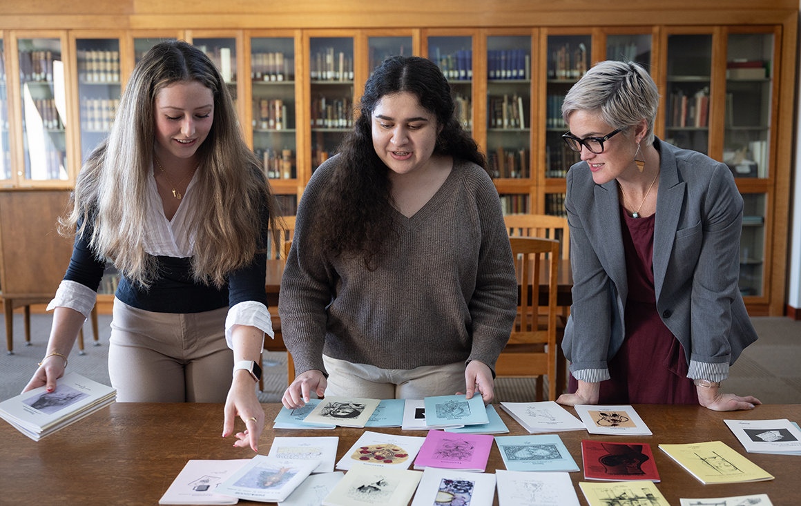 Two students and a teacher examine an array of zines in a library archive.