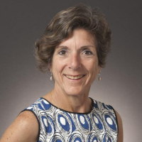 A woman smiling wearing a patterned dress against a neutral background.