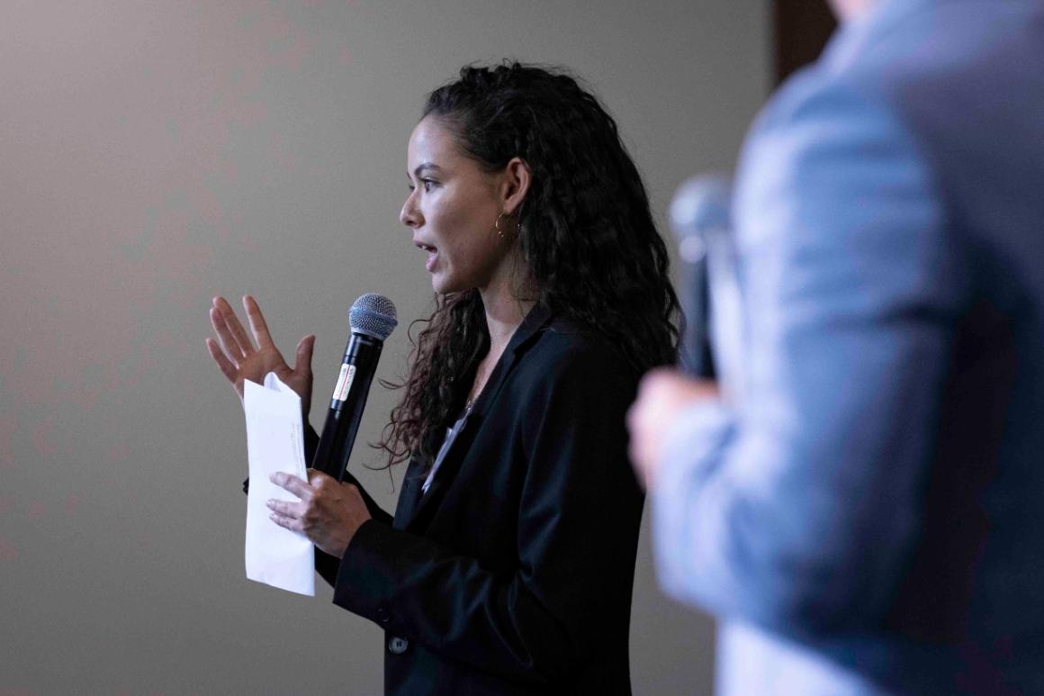 A person speaking into a microphone, holding a paper.