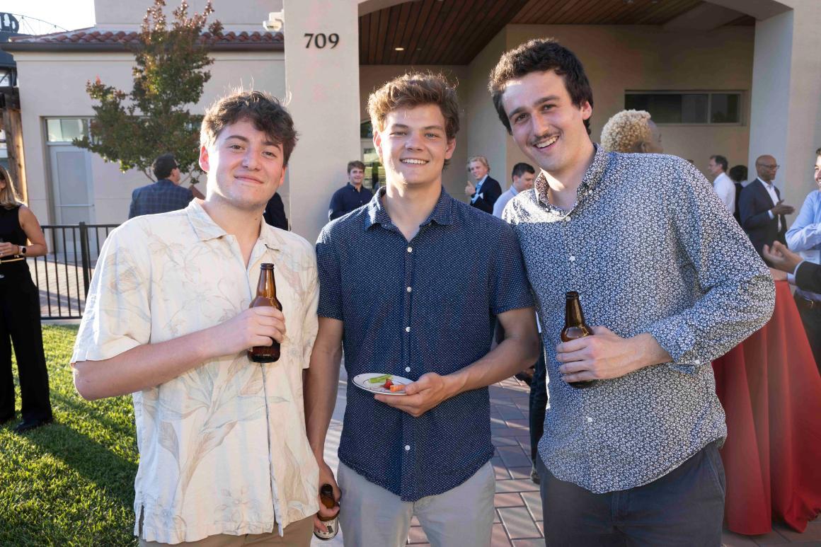 Three people holding drinks at an outdoor gathering.