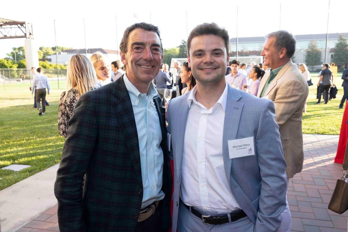 Two men in suits attending an outdoor social event.