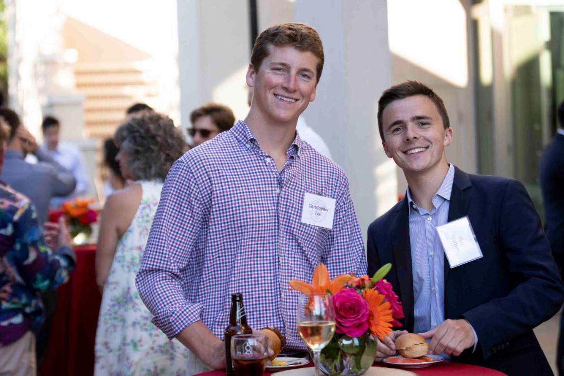 Two men smiling at an outdoor event, with name tags attached to their shirts.