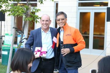 Two men smiling and holding award trophy plaques outdoor.