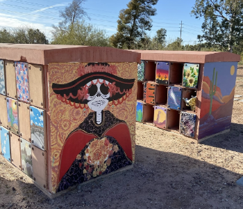 Colorful painted utility boxes outdoors with various artistic designs, including a character with a red hat.