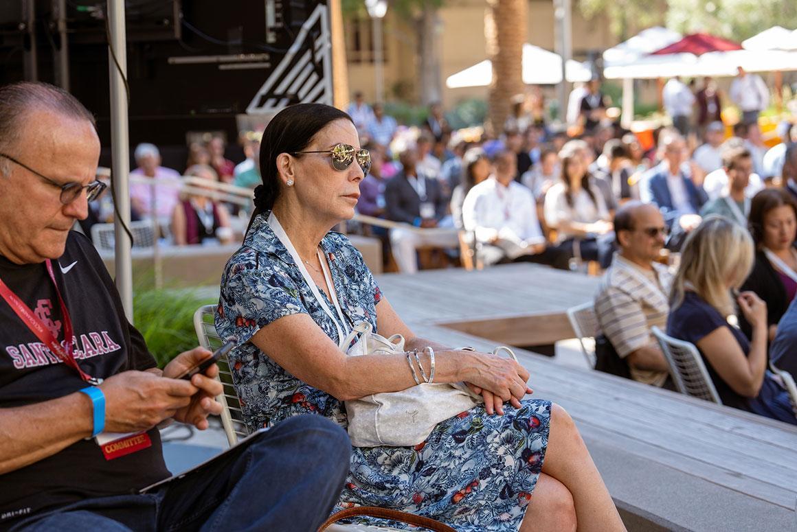 People sitting at an outdoor event with a crowd in the background.