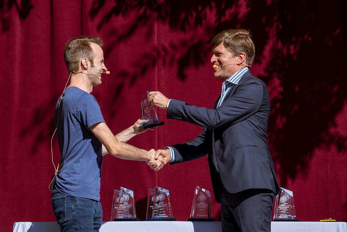 Two people shaking hands on stage with a red curtain background.