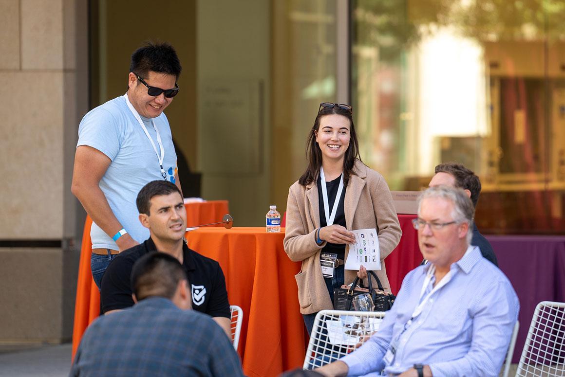 People interacting at an outdoor event with orange tablecloths.