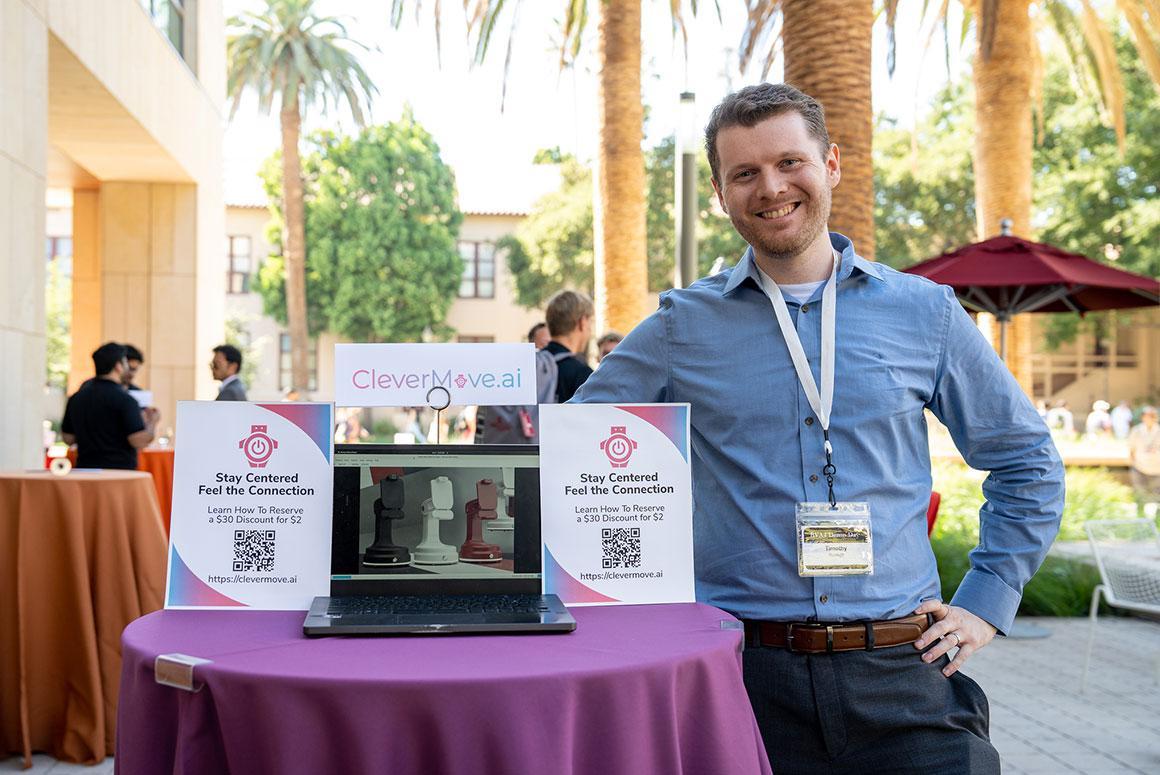 Person at demo booth with laptop and informational signs on a purple table.