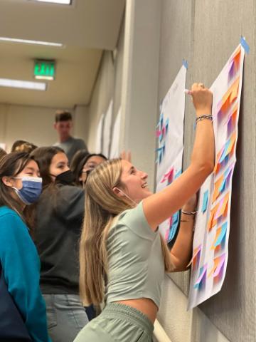 A person pinning ideas on a board with a group watching nearby.