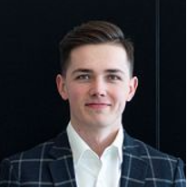 A person in a checked blazer in front of a dark background.